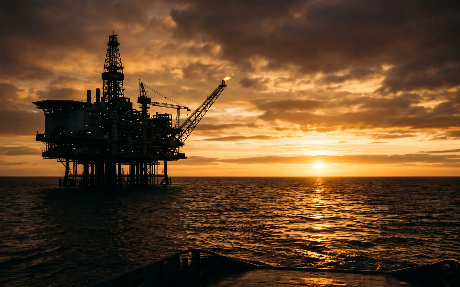 Offshore oil platform silhouetted against a sunset over open sea